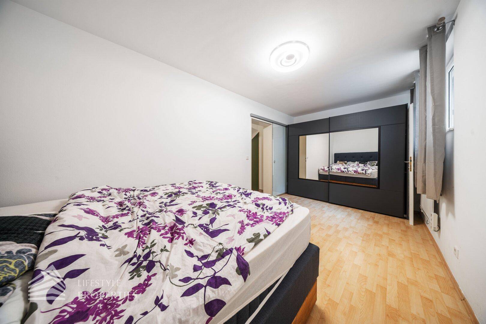 Geräumiges Schlafzimmer mit Doppelbett, Spiegelschiebetüren und hellem Boden.