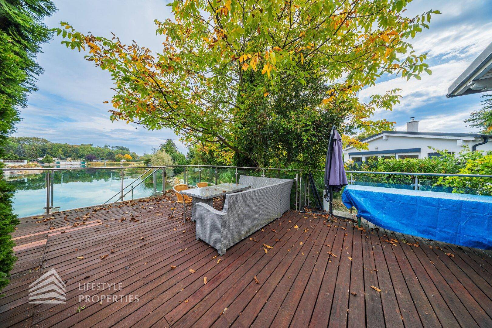 Gemütliche Holzterrasse mit Lounge-Möbeln und direktem Blick auf den See.
