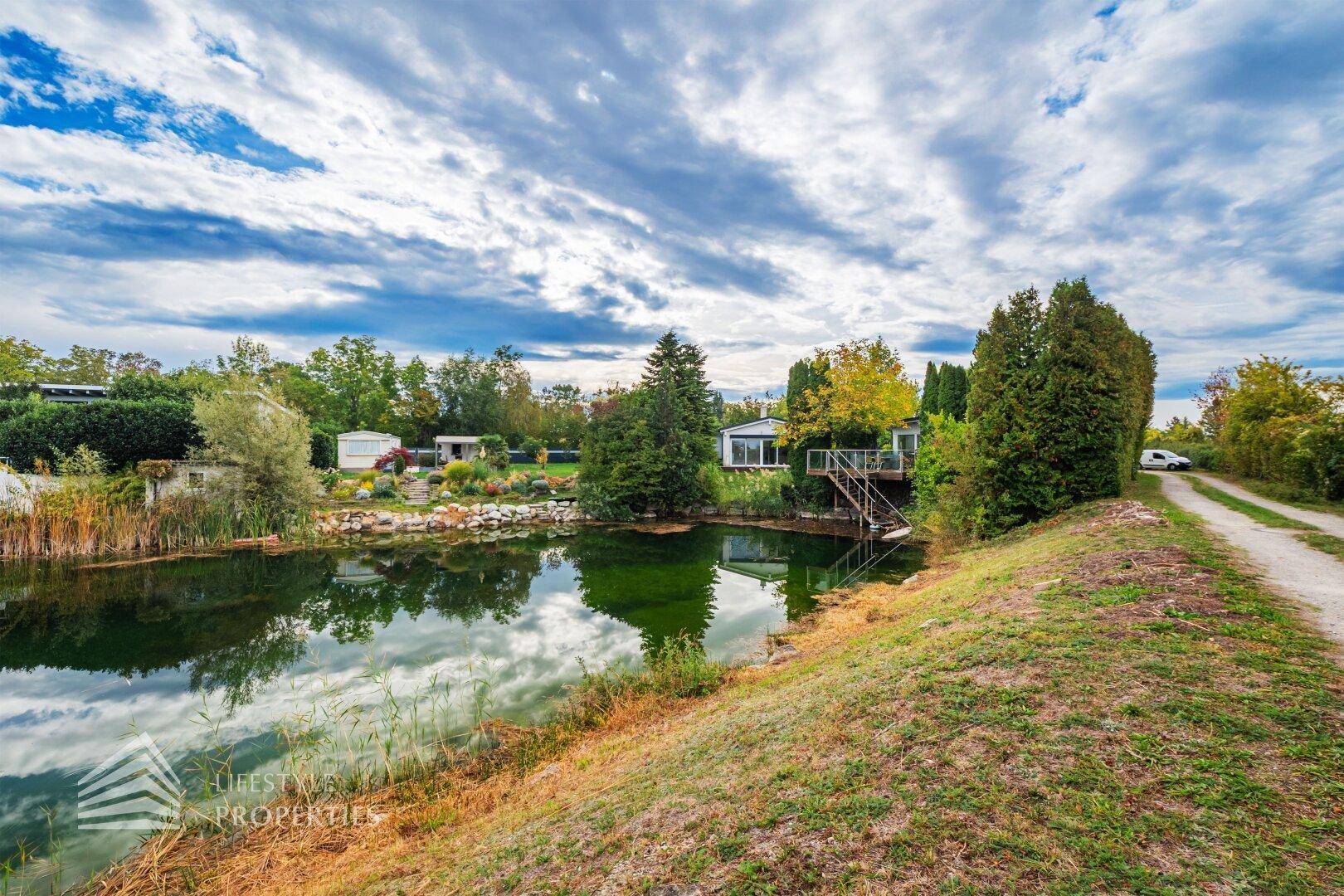 Malerischer Blick auf einen Teich mit einem Haus am gegenüberliegenden Ufer und üppiger Natur.