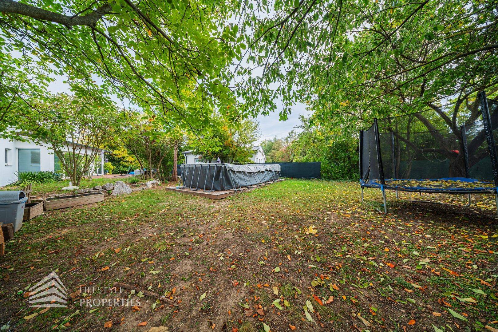 Weitläufiger Garten mit oberirdischem Pool, Trampolin und altem Baumbestand für Freizeitaktivitäten.