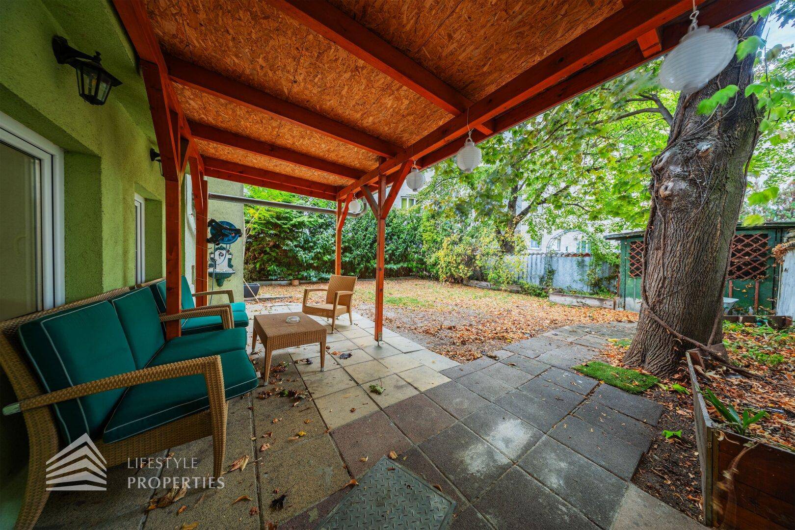 Überdachte Terrasse mit Sitzgelegenheiten und Blick auf den Garten mit Bäumen.