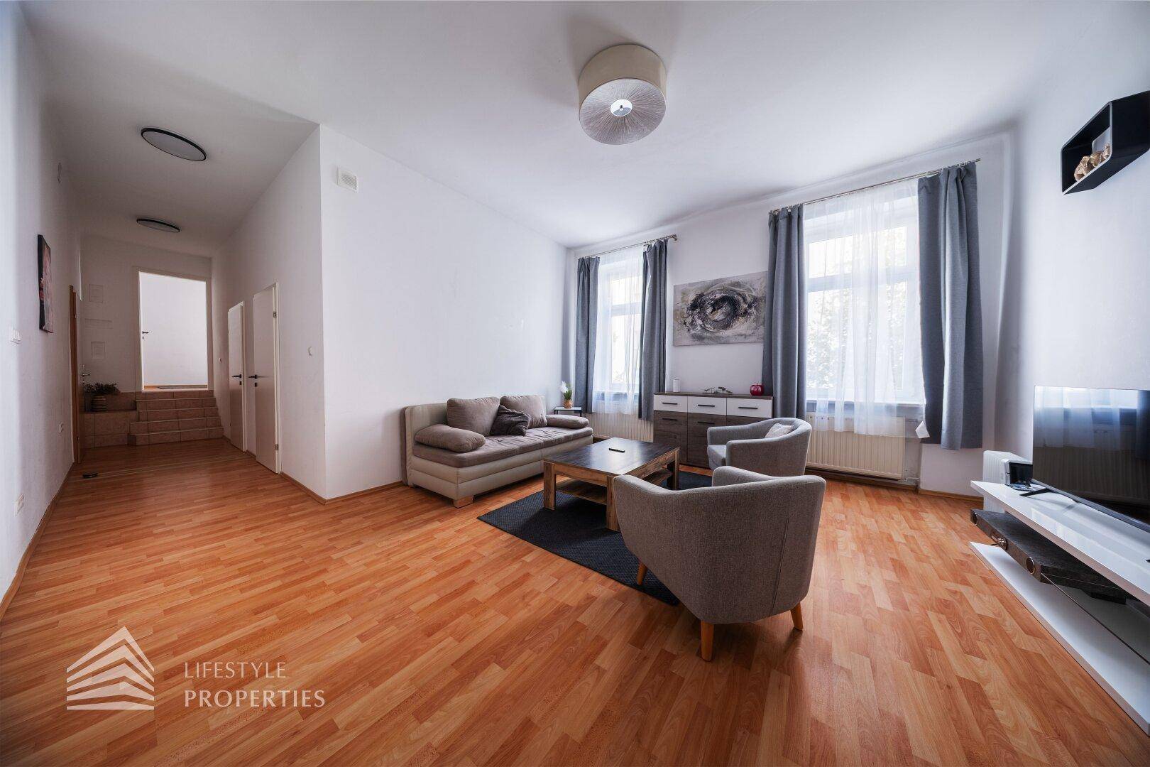 Gemütliches Wohnzimmer mit Holzboden, beigen Sofas und Blick auf die Straße.