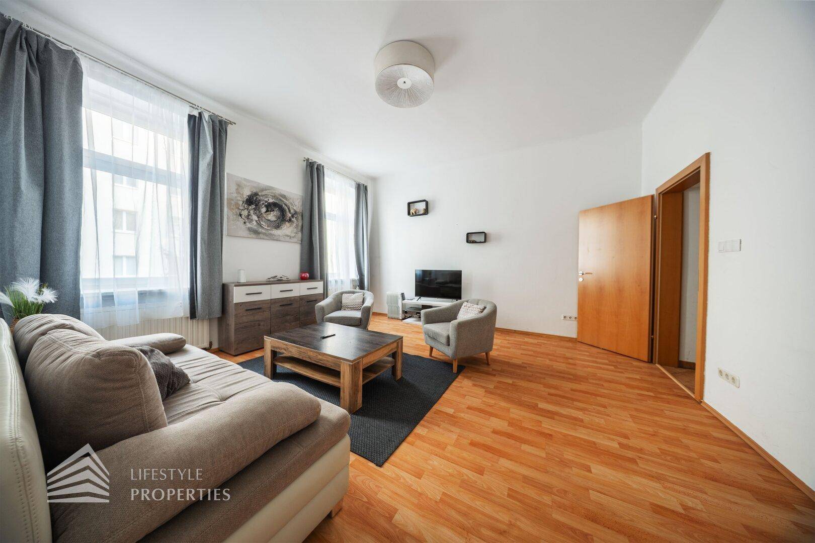 Helles Wohnzimmer mit Holzboden, bequemen Sitzgelegenheiten und einem Fernseher.