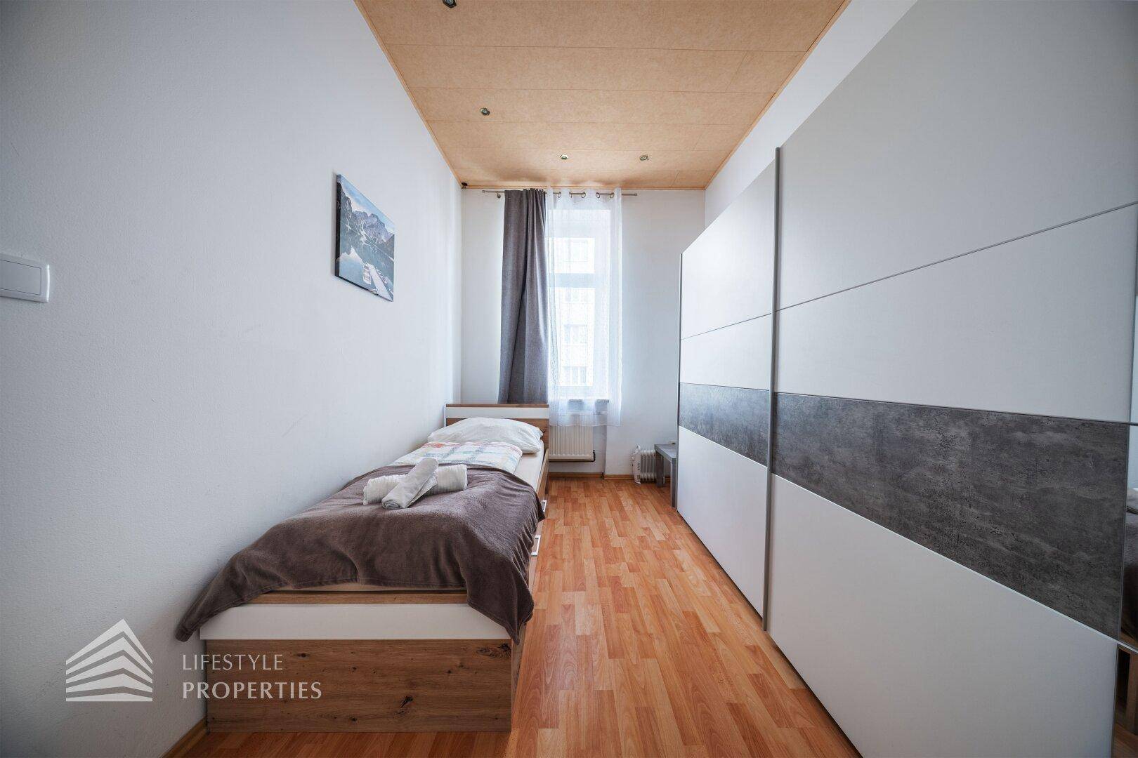Gemütliches Schlafzimmer mit Einzelbett, Holzboden und großem Kleiderschrank.