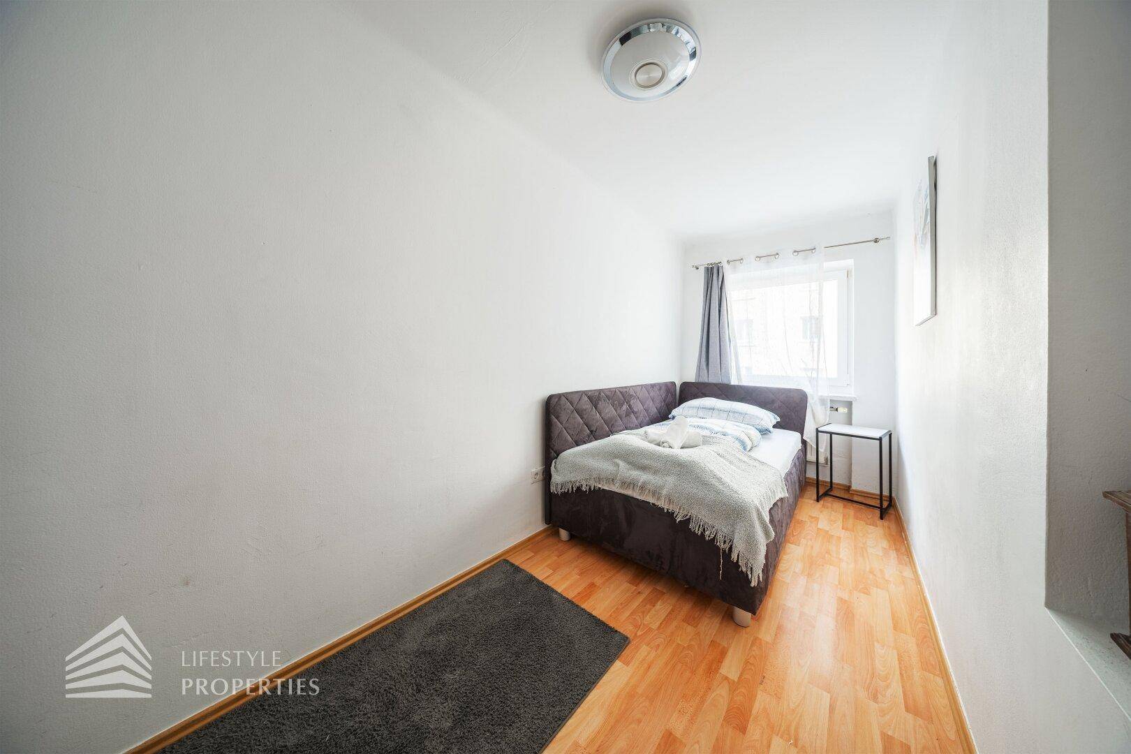 Einfaches Schlafzimmer mit Doppelbett, Holzboden und einem kleinen Fenster.