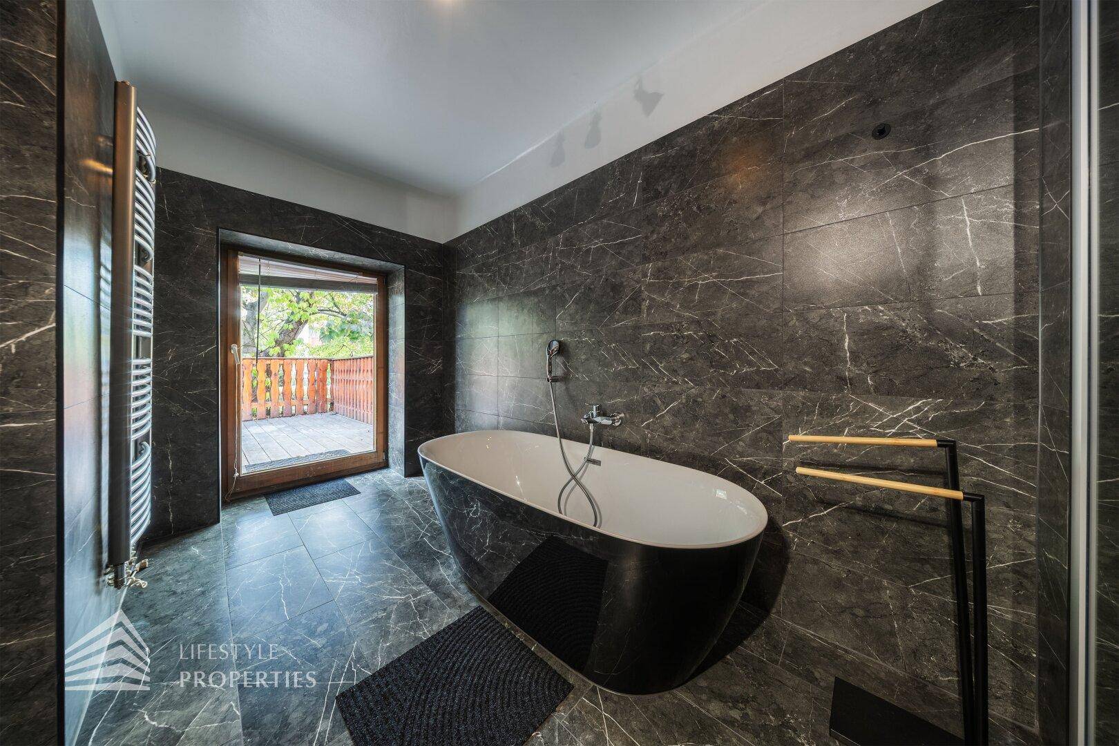 Elegantes Badezimmer mit freistehender Badewanne, dunklen Marmorfliesen und Zugang zur Terrasse.