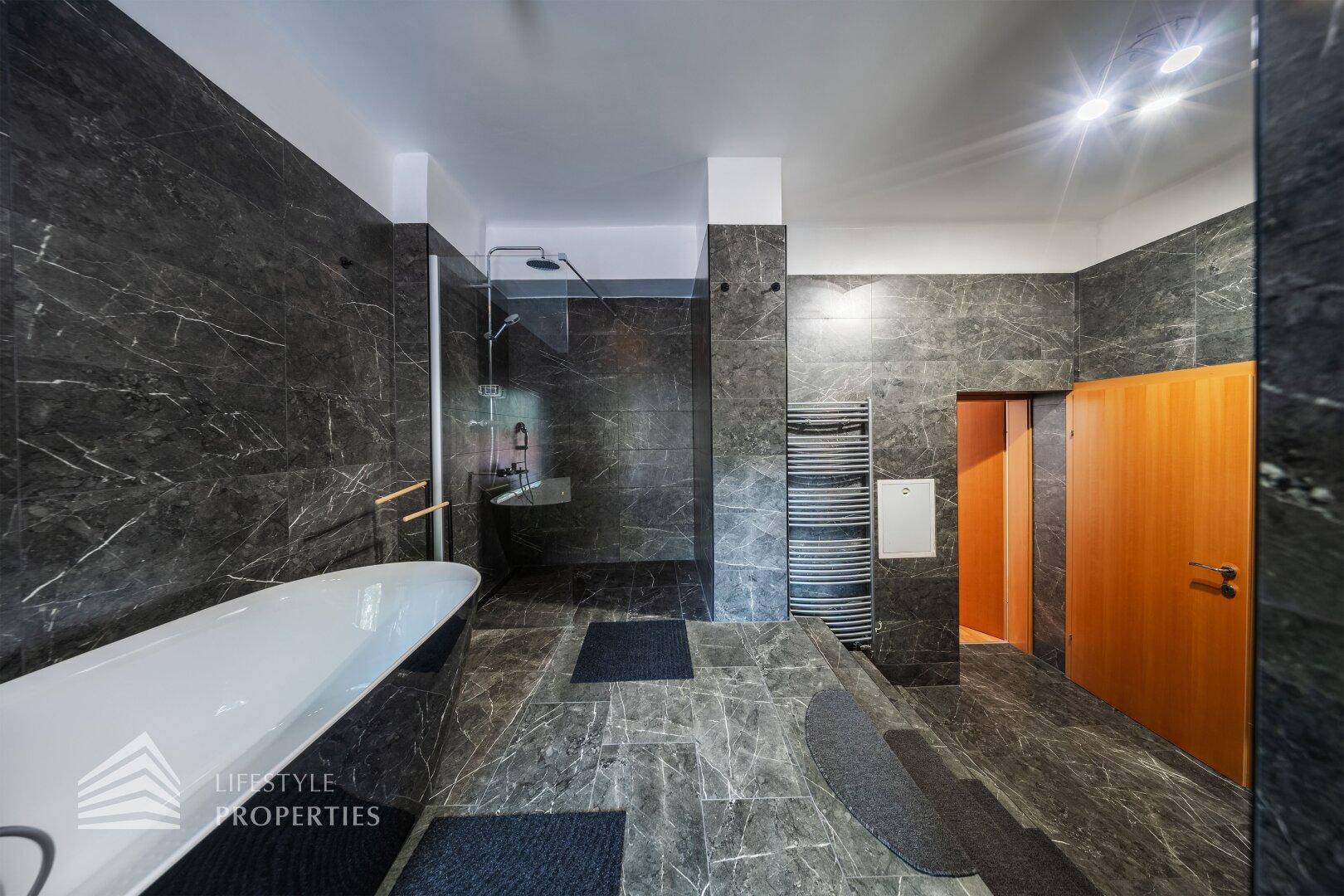 Geräumiges Badezimmer mit dunklen Marmorfliesen, freistehender Badewanne und begehbarer Dusche.