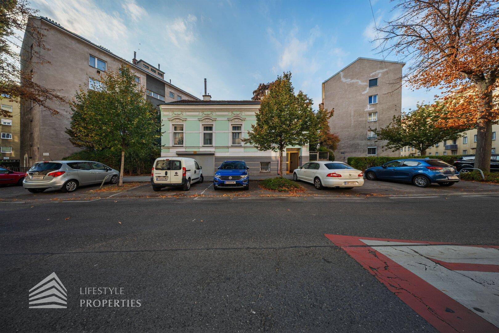 Straßenansicht eines Gebäudes mit Parkplätzen und umliegenden Häusern.