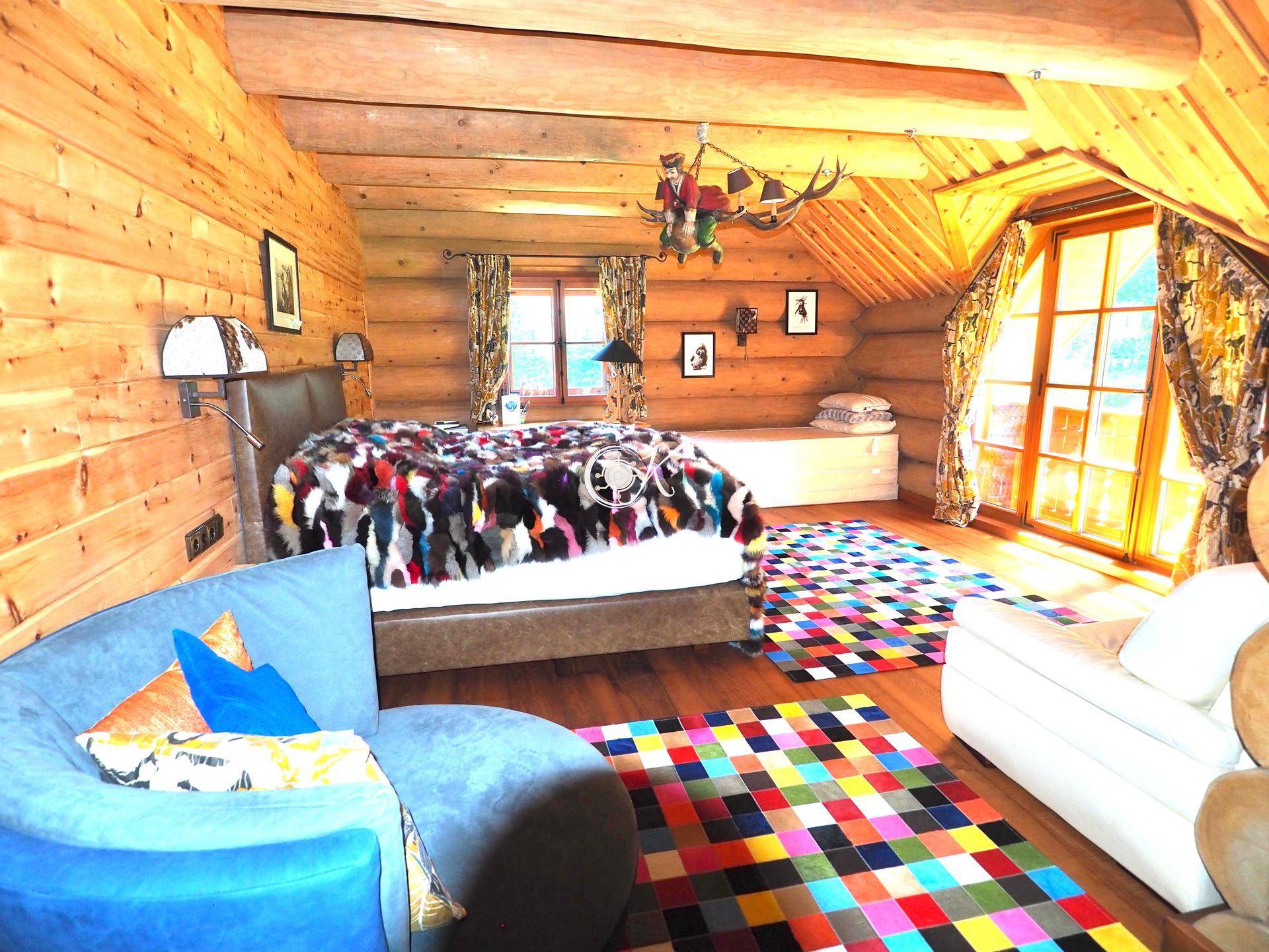 Farbenfrohes Schlafzimmer im Dachgeschoss mit Holzwänden, Holzboden und einem großen Fenster.