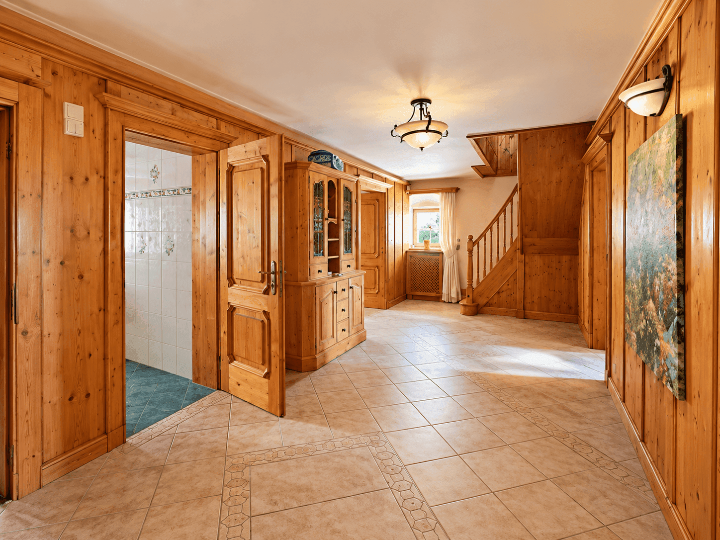 Geräumiger Flur mit Holzvertäfelung, Fliesenboden und einer Holztreppe, die in die obere Etage führt.