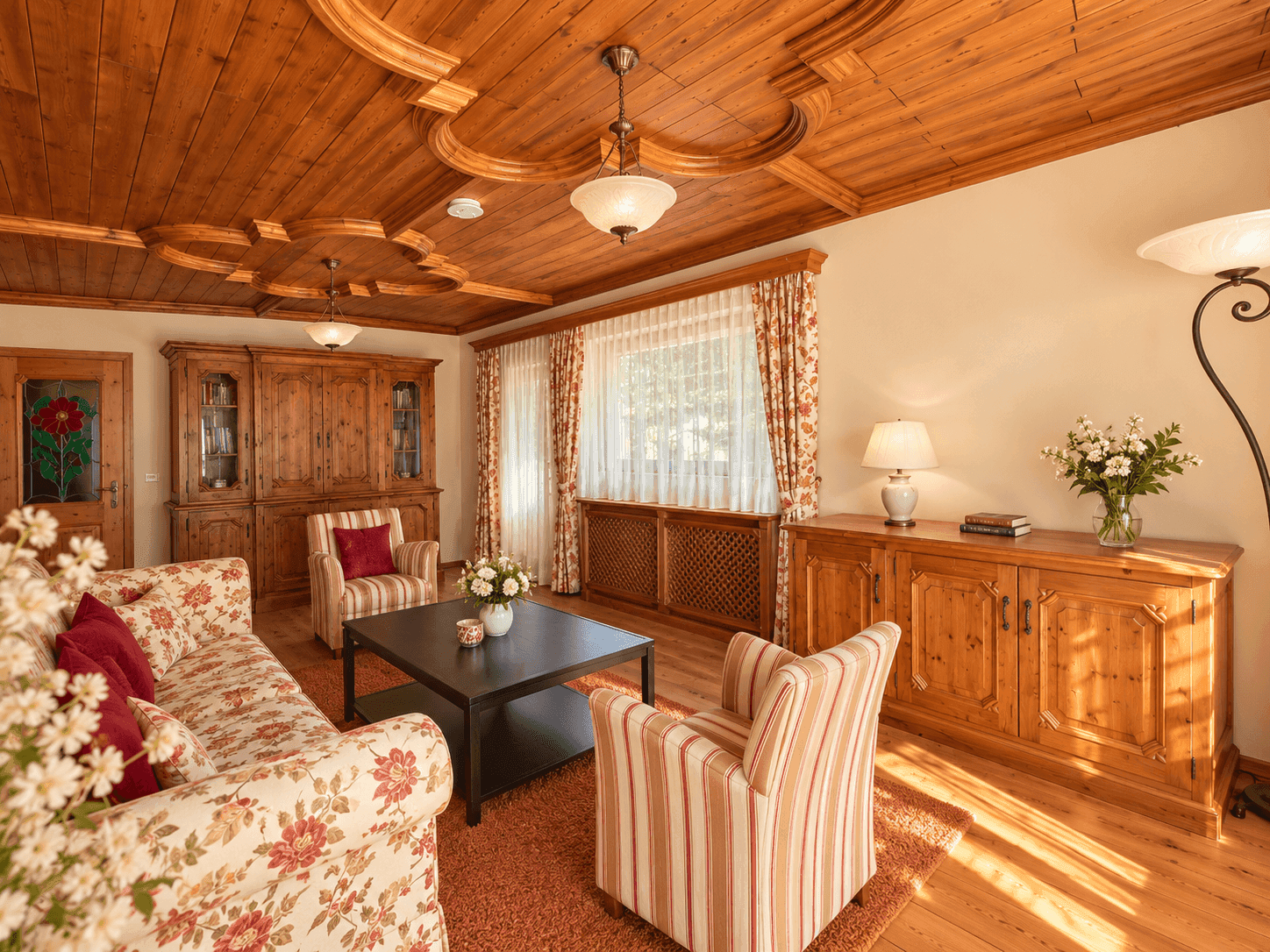 Traditionelles Wohnzimmer mit Holzbalkendecke, floralen Sofas und Blick ins Grüne.