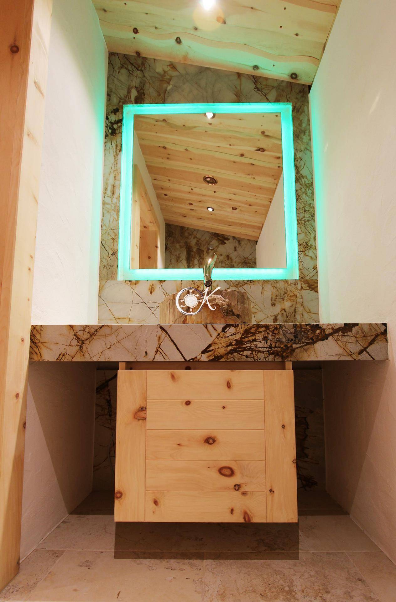 Modernes Badezimmer mit beleuchtetem Spiegel, Holzwaschtisch und Steinplatte.