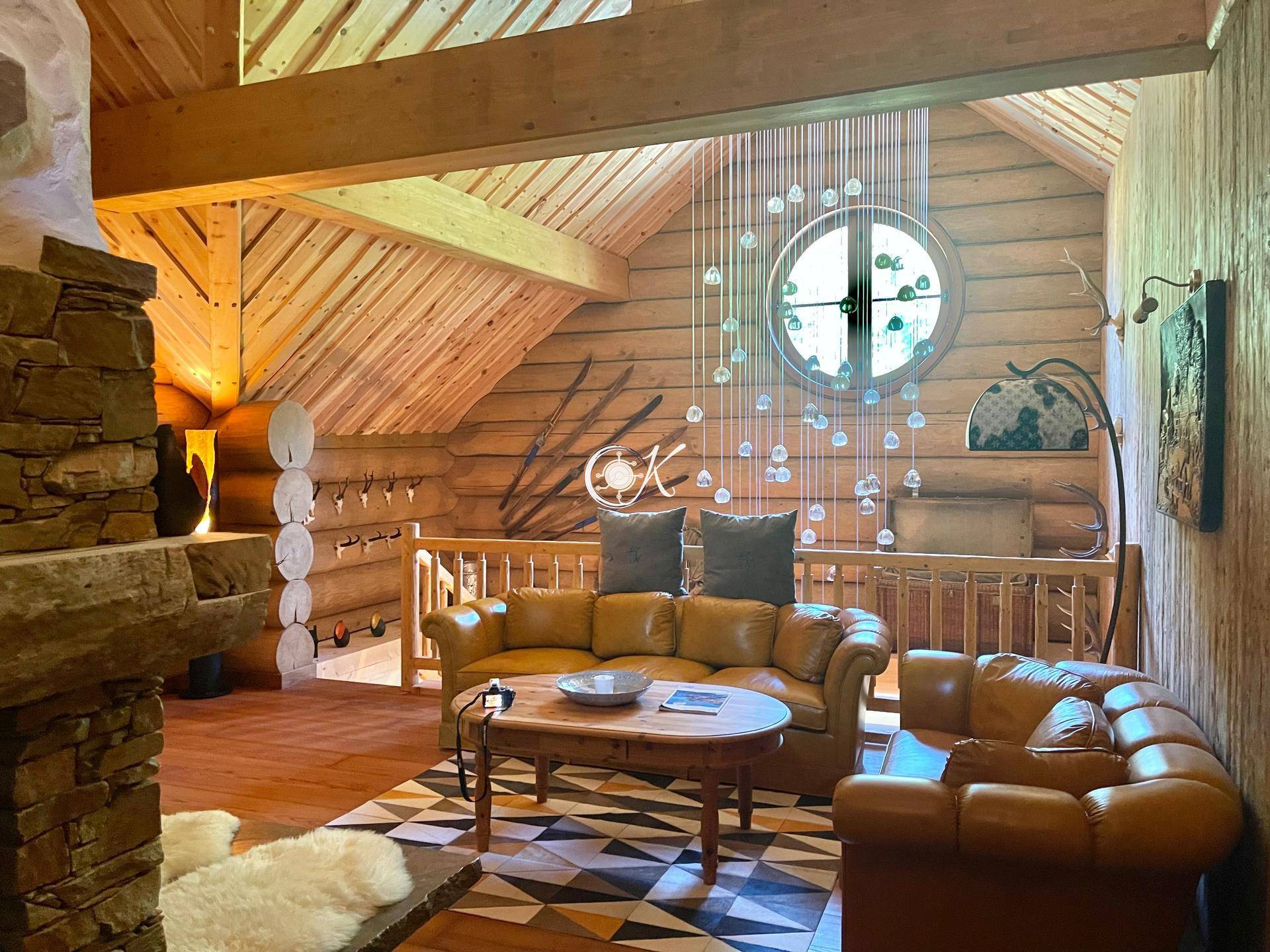 Rustikales Wohnzimmer mit Ledersofas, Holzwänden und einer Galerie mit Blick auf den Wohnbereich.