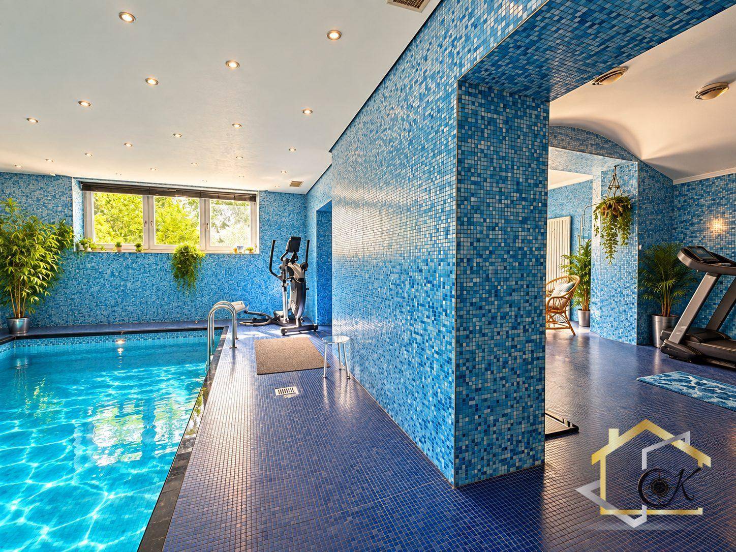Großzügiger Wellnessbereich mit Hallenbad, blauen Mosaikfliesen und Fitnessgeräten.