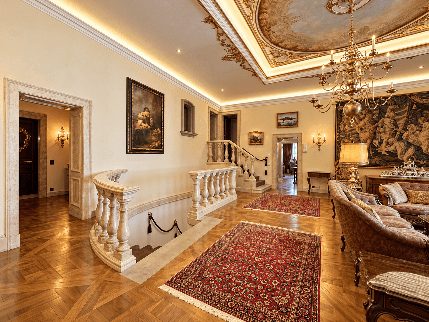 Repräsentativer Wohnbereich mit Fischgrätparkett, kunstvoller Decke und einer geschwungenen Marmortreppe.