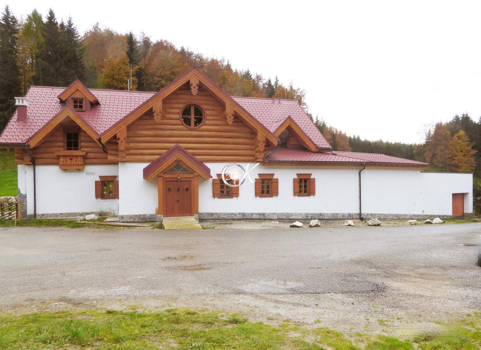 Traditionelles Holzhaus mit weißer Fassade, rotem Dach und rustikalen Holzelementen in ländlicher Umgebung.
