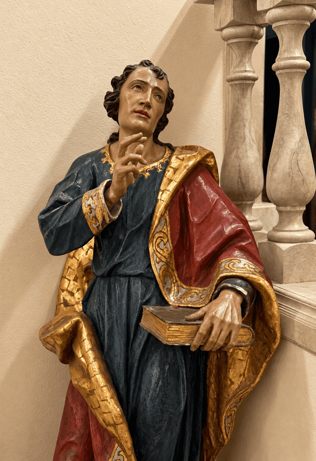 Detailaufnahme einer klassischen Statue mit Buch und einer Balustrade im Hintergrund.