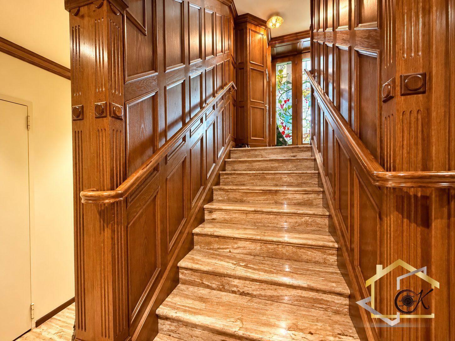Elegante Treppe mit aufwendiger Holzvertäfelung und farbigem Glasfenster, die zu den oberen Etagen führt.