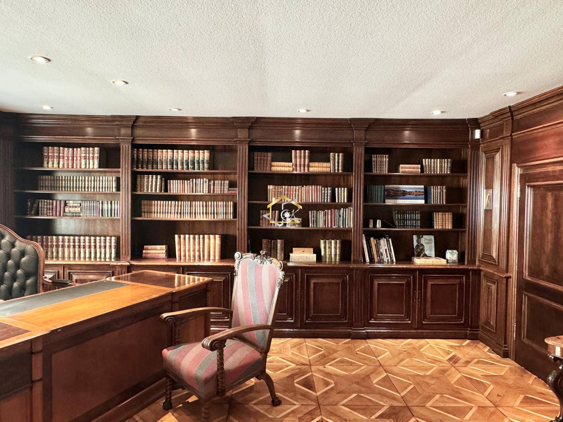 Elegantes Arbeitszimmer mit raumhohen Bücherregalen, Holzvertäfelung und Parkettboden.