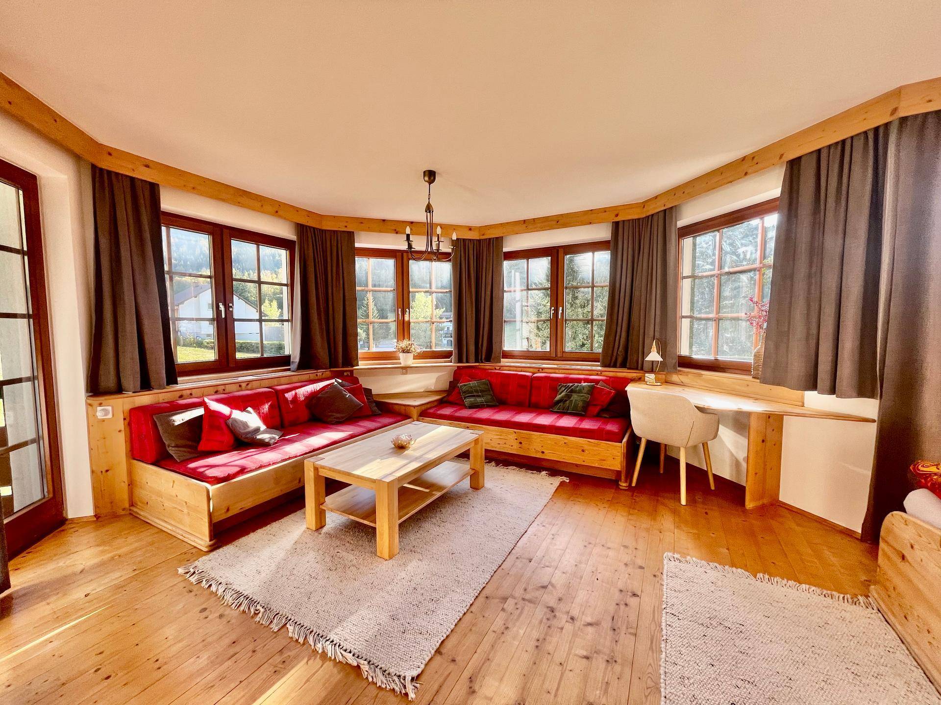 Gemütliches Wohnzimmer mit Holzboden, eingebauten Sitzbänken und vielen Fenstern für viel Tageslicht.