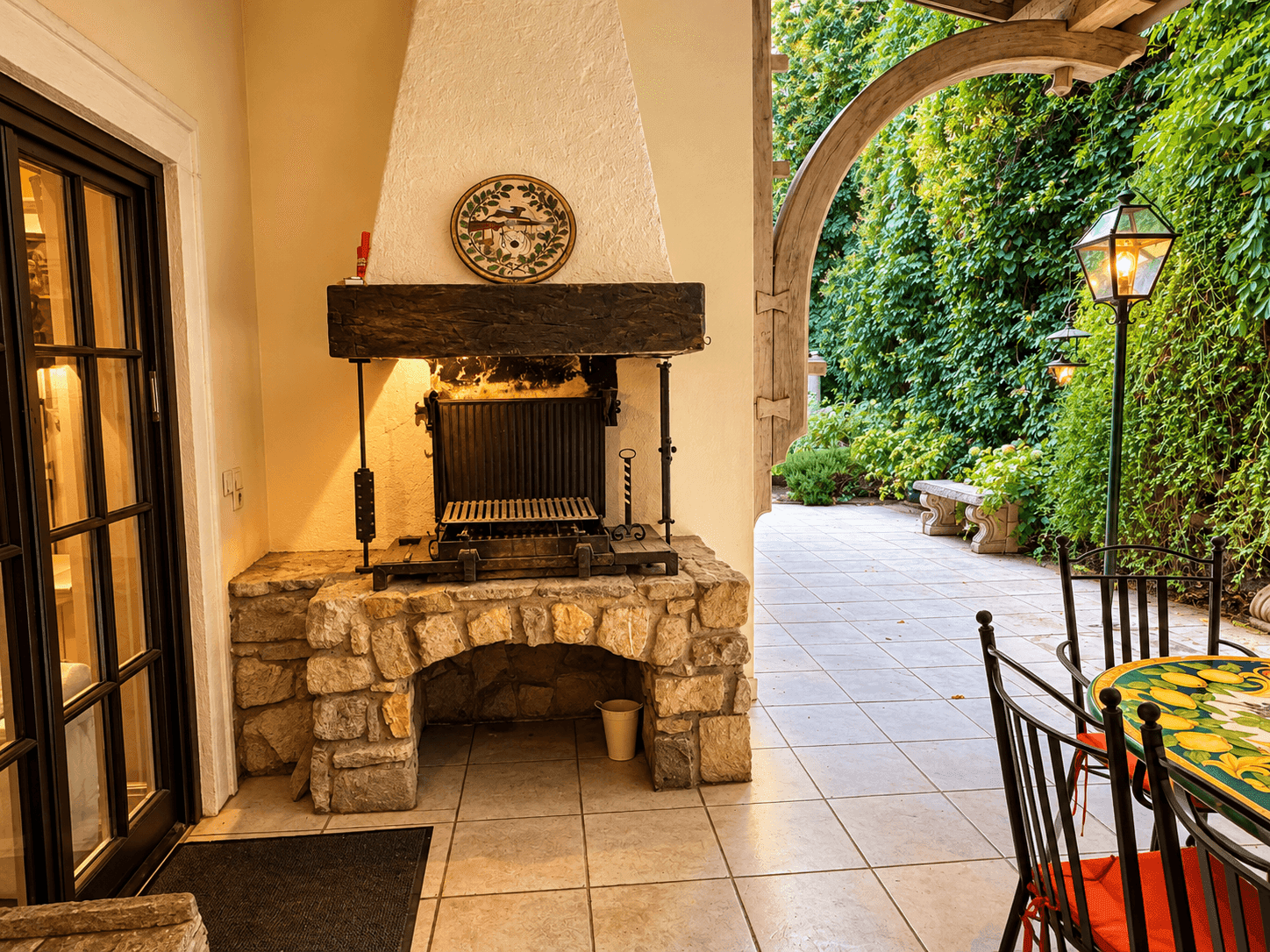 Überdachte Terrasse mit gemauertem Grillplatz, Fliesenboden und Sitzgelegenheiten im Freien.