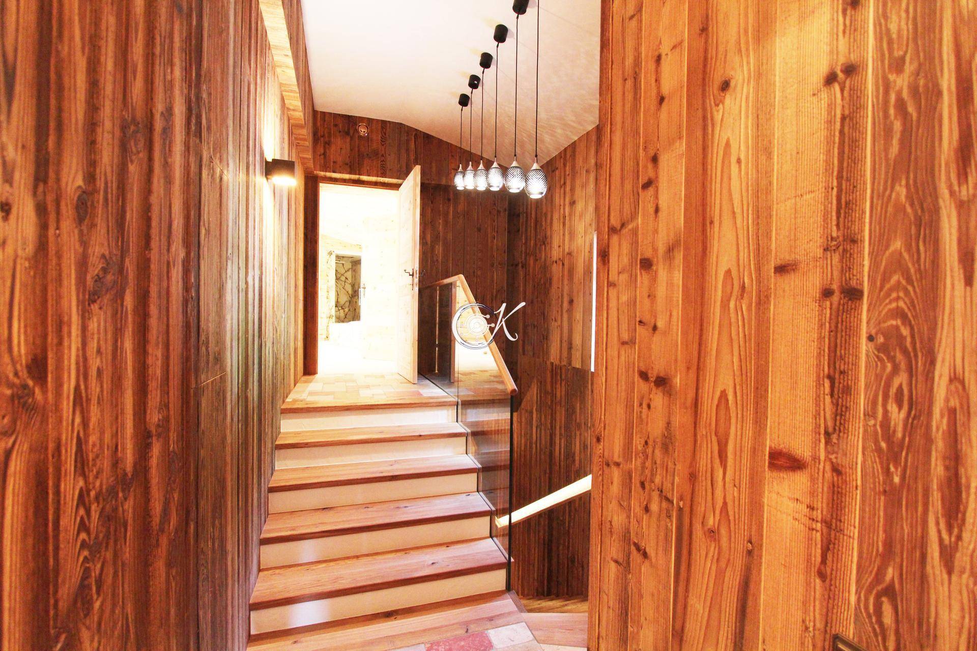 Rustikaler Flur mit Holzwänden, Holztreppe und moderner Beleuchtung.