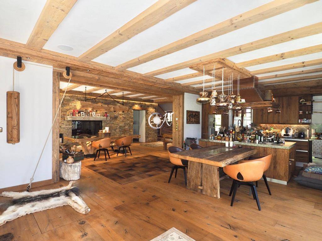 Offener Wohn- und Essbereich mit rustikalem Holztisch, Steinwand und gemütlicher Atmosphäre.