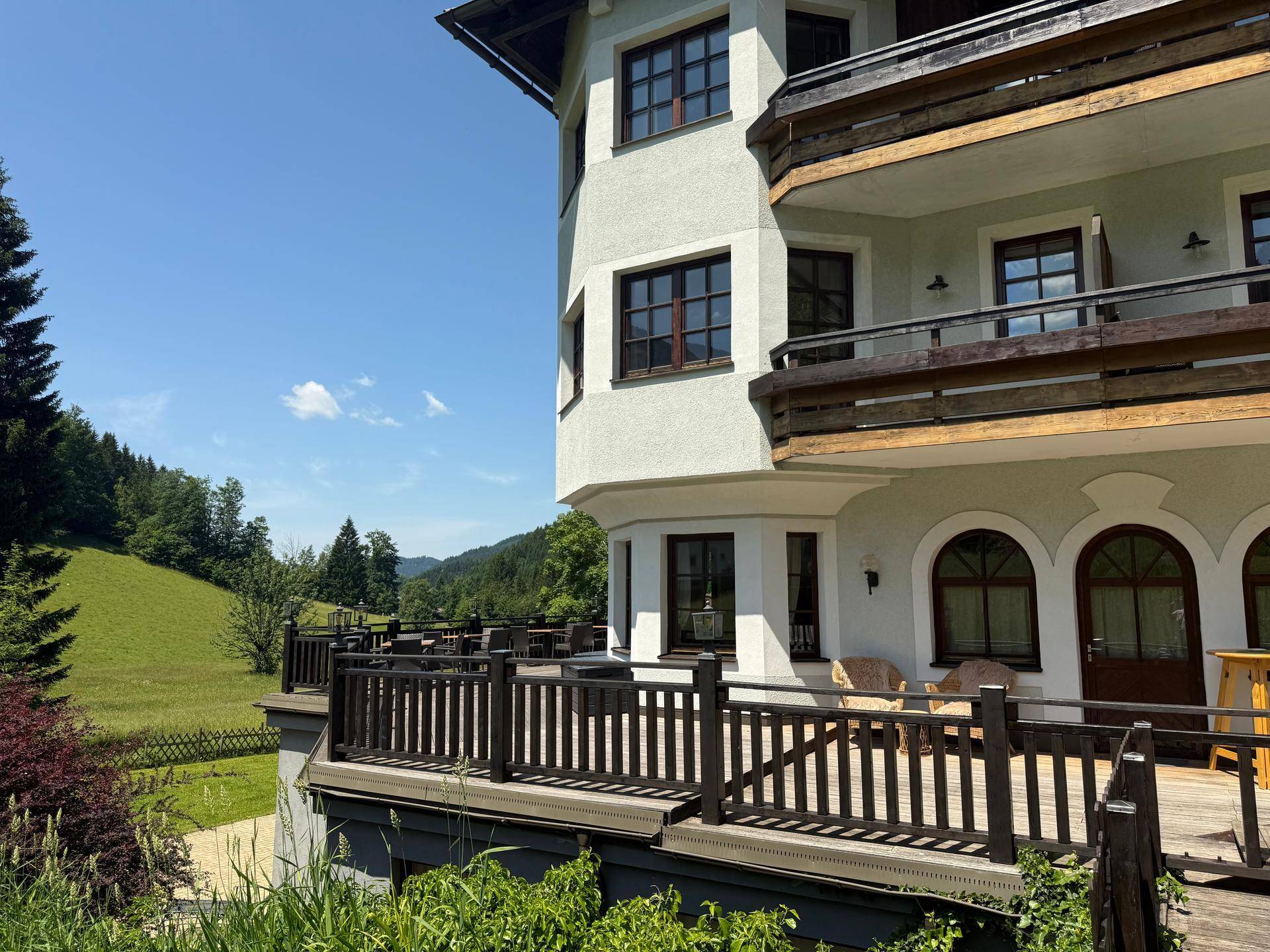 Seitenansicht des Gebäudes mit einer großen Holzterrasse und Blick auf die grüne Landschaft.