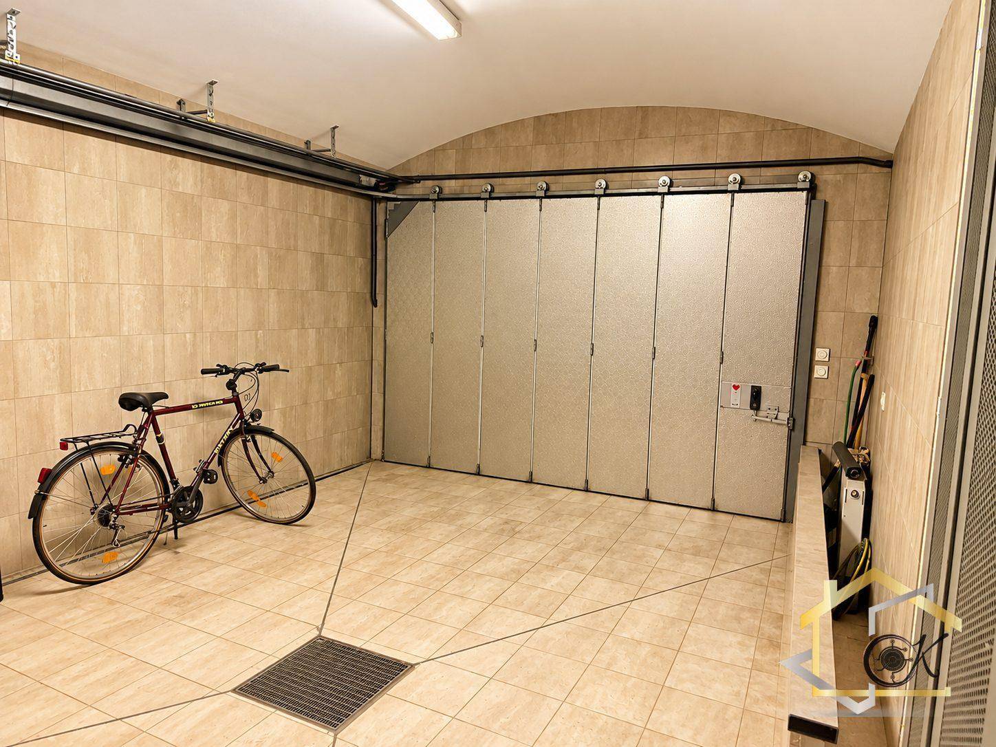 Geräumige Garage mit Fliesenboden, Falttor und Platz für Fahrräder und Fahrzeuge.