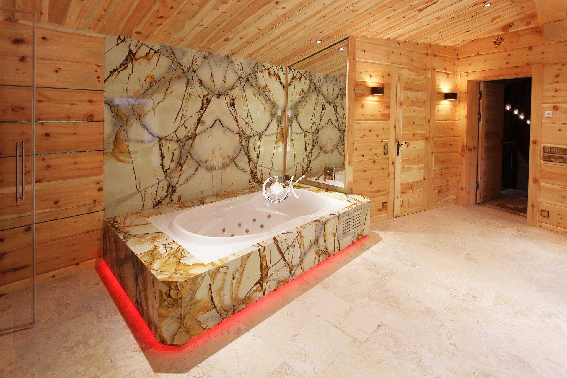 Luxuriöses Badezimmer mit Whirlpool-Badewanne, Steinverkleidung und indirekter Beleuchtung.