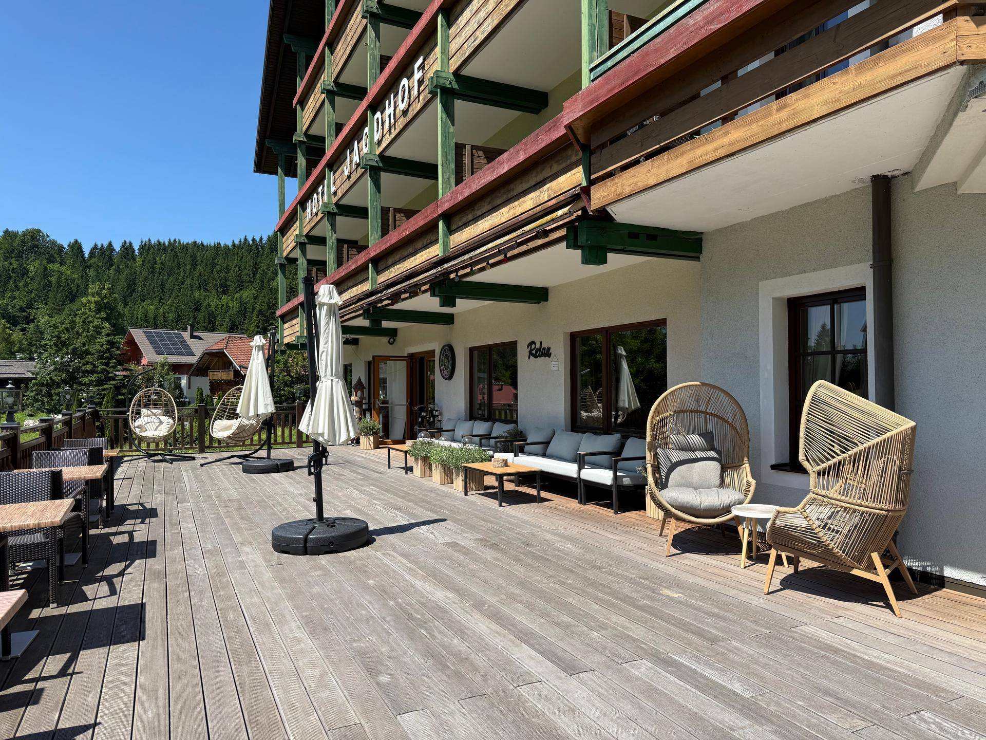 Große Holzterrasse mit verschiedenen Sitzgelegenheiten und Sonnenschirmen vor dem Gebäude.
