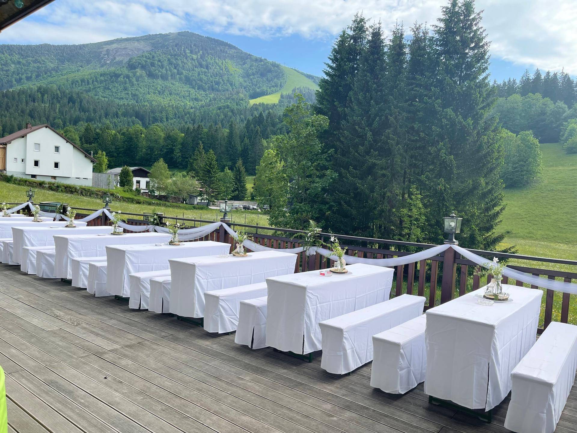 Festlich gedeckte Tische und Bänke auf einer Holzterrasse mit Bergblick.