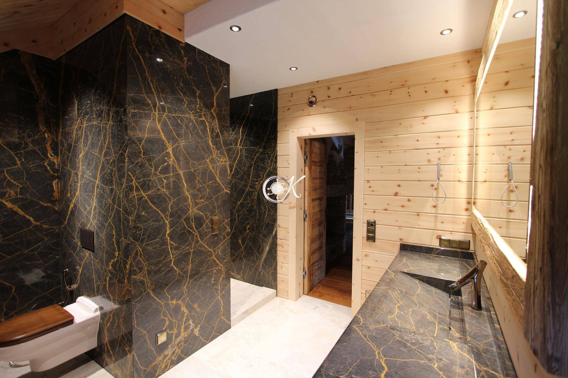 Modernes Badezimmer mit dunkler Steinwand, Holzwaschtisch und beleuchtetem Spiegel.
