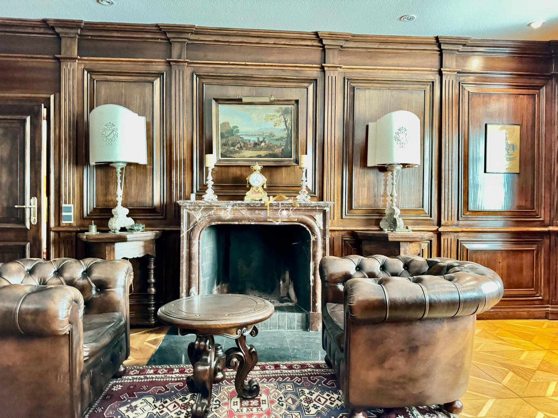 Elegantes Wohnzimmer mit dunkler Holzvertäfelung, Chesterfield-Sesseln und Marmorkamin.