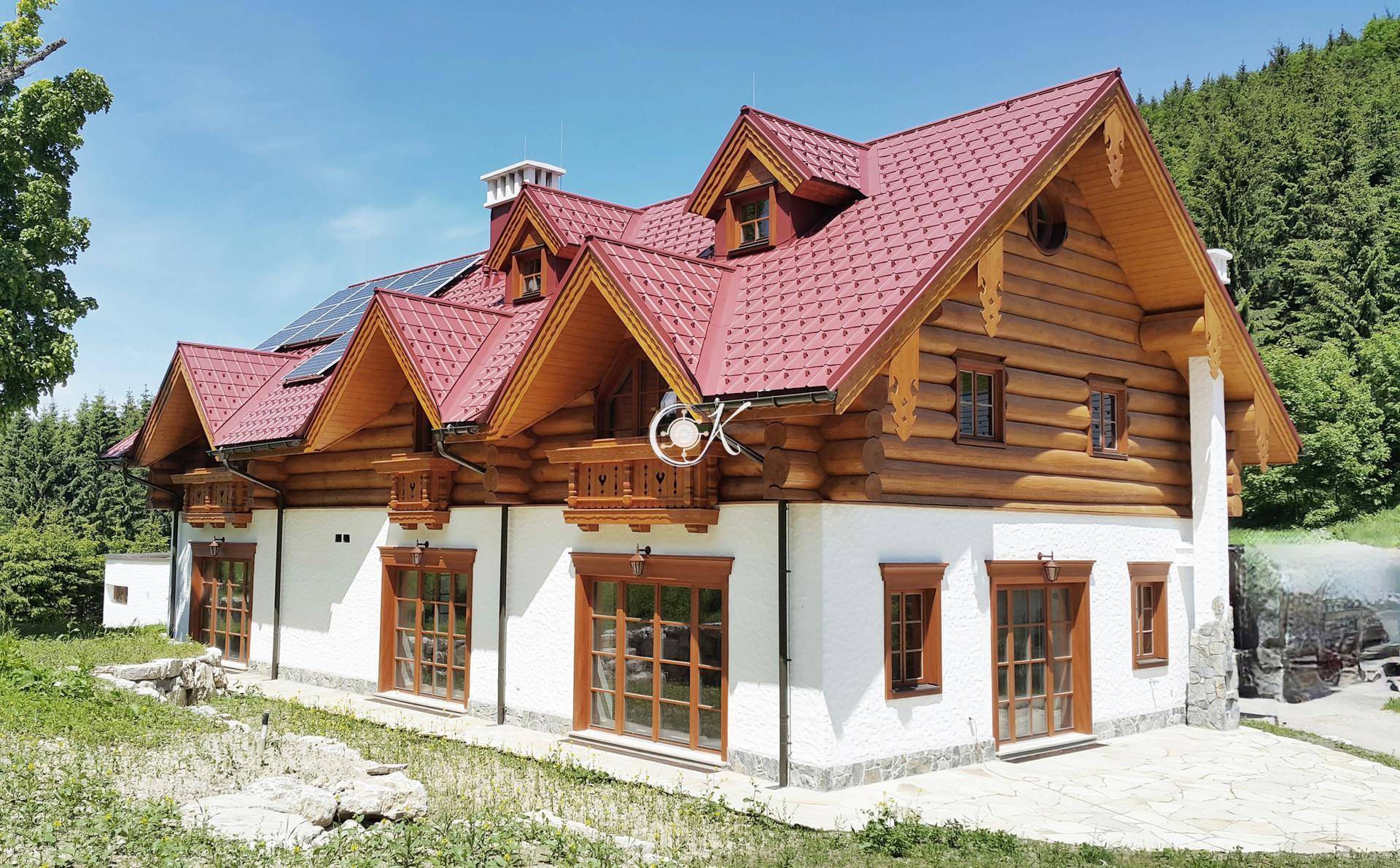 Traditionelles Holzhaus mit weißer Fassade, rotem Dach und rustikalen Holzelementen in sonniger Umgebung.