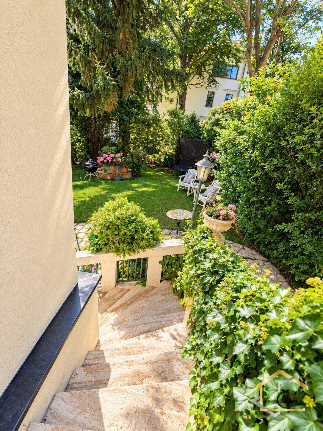 Steintreppe führt hinunter in einen gepflegten Garten mit üppiger Vegetation und Sitzgelegenheiten.