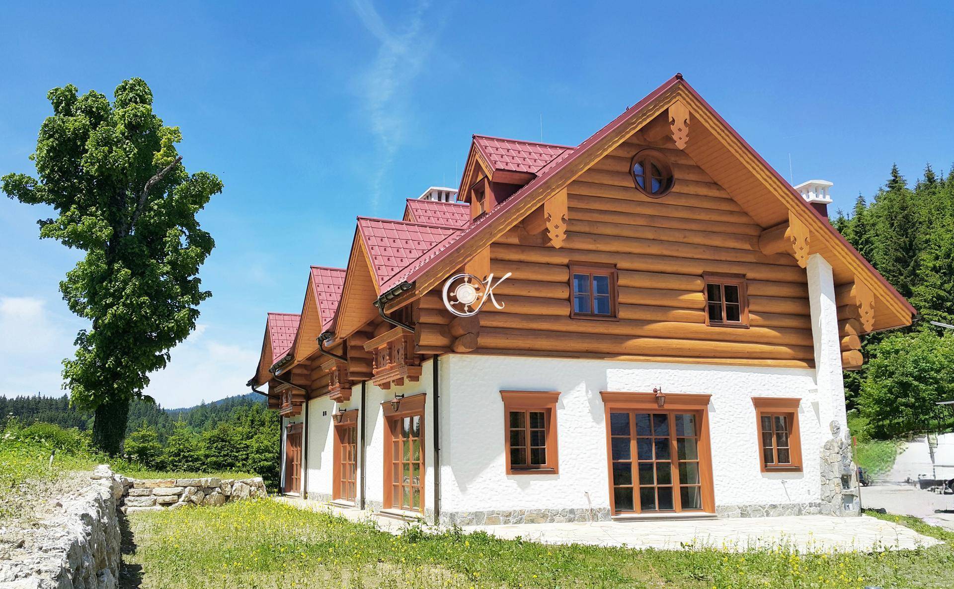 Traditionelles Holzhaus mit weißer Fassade, rotem Dach und rustikalen Holzelementen in sonniger Umgebung.