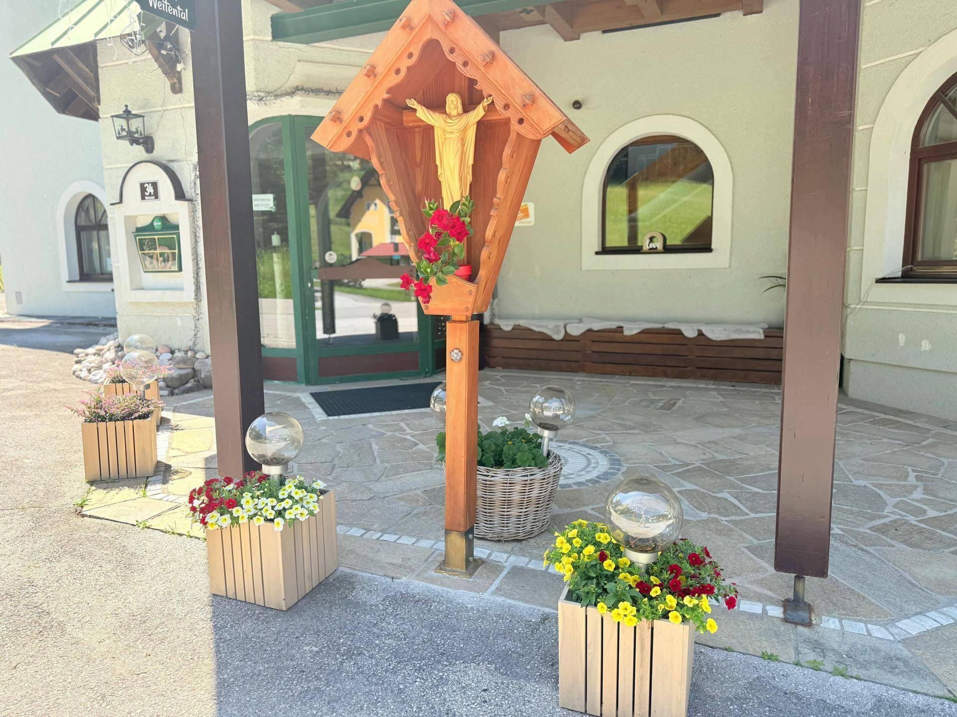 Dekorative Blumenkübel und ein Holzkreuz vor dem Eingang eines Gebäudes.