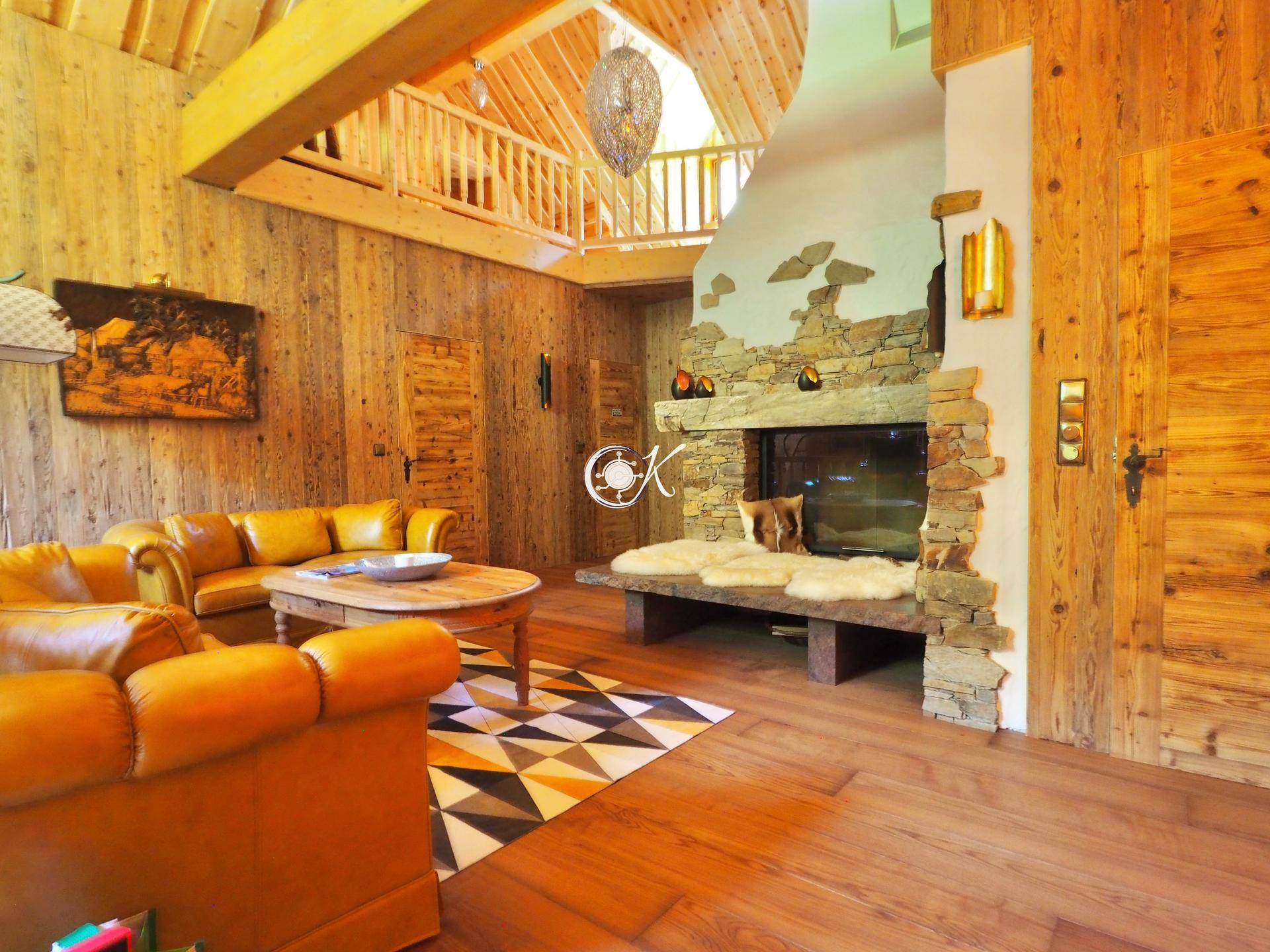 Gemütliches Wohnzimmer im Chalet-Stil mit Ledersofas, Holzwänden und einem steinernen Kamin.