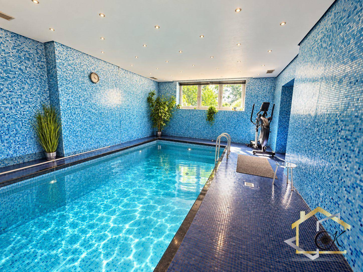 Hallenbadbereich mit blauen Mosaikfliesen, Schwimmbecken und Fitnessgeräten.