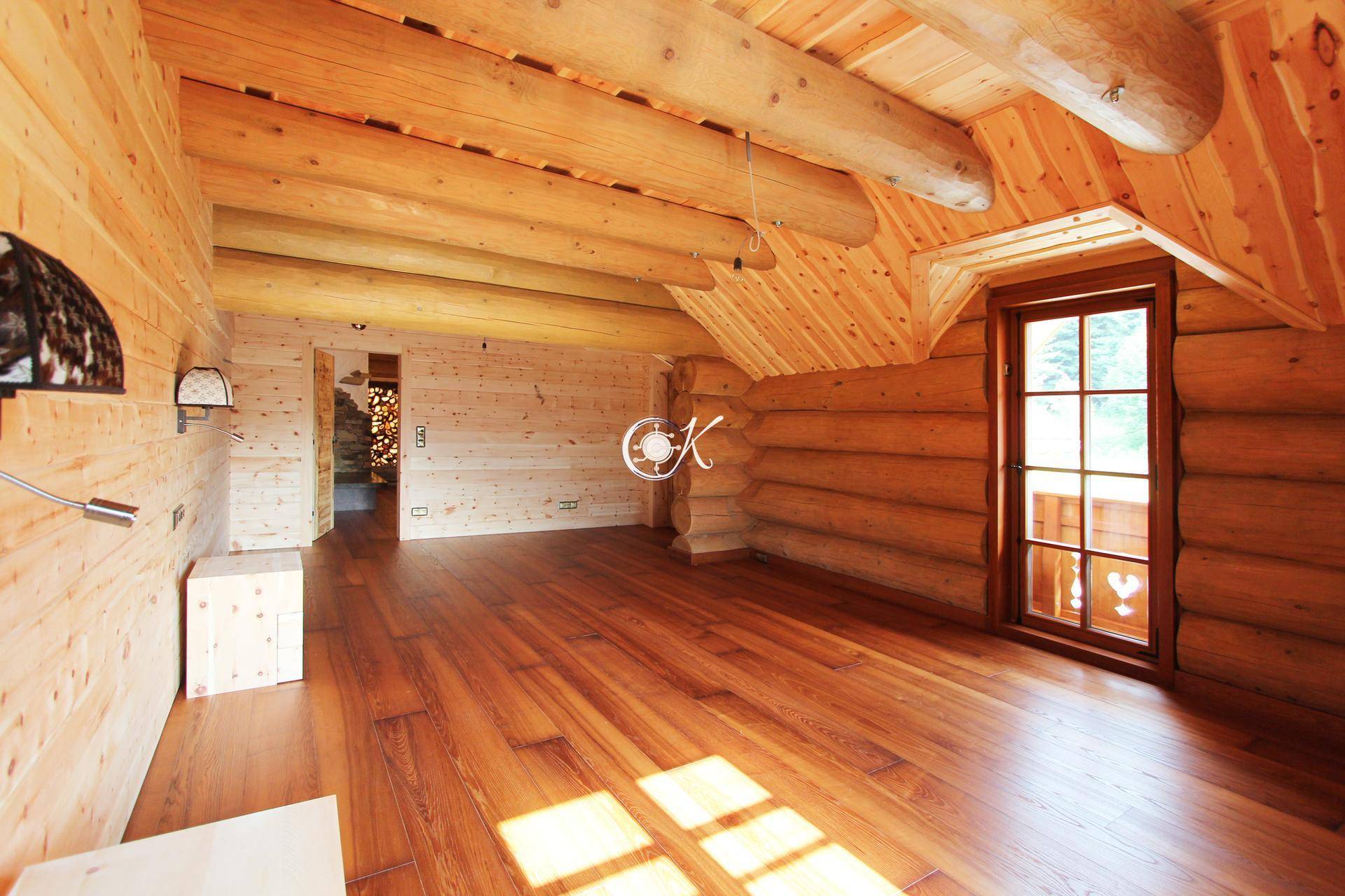 Helles Zimmer mit Holzwänden und -decke, Holzboden und einem großen Fenster.