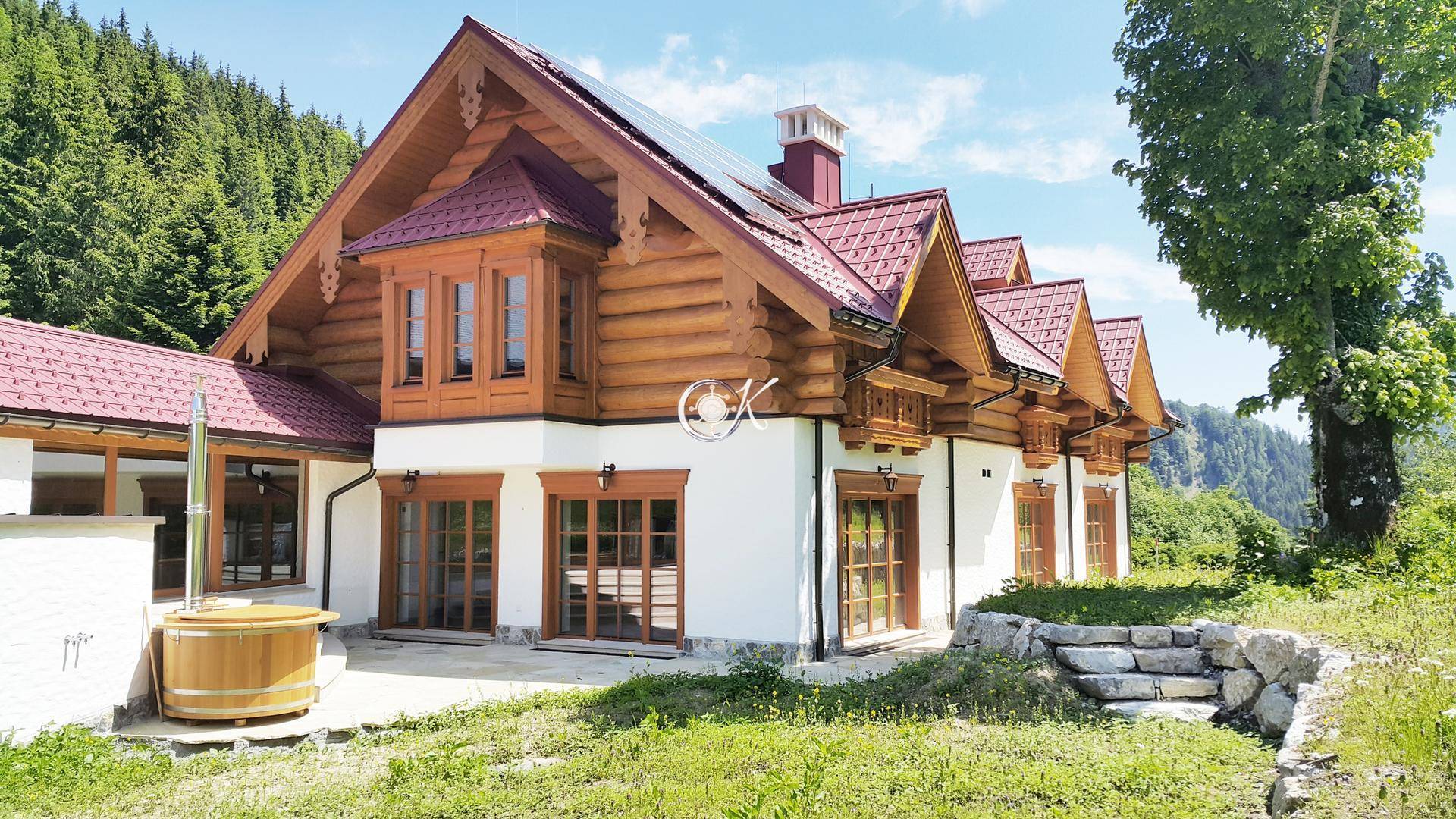 Traditionelles Holzhaus mit weißer Fassade, rotem Dach und rustikalen Holzelementen in sonniger Umgebung.