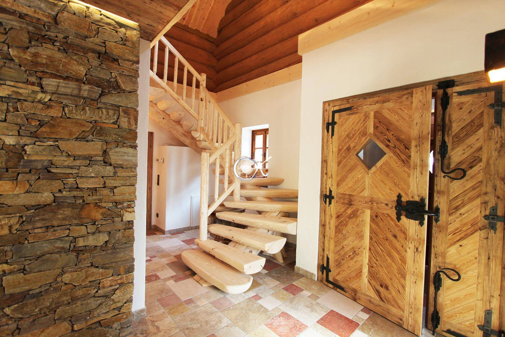 Rustikaler Eingangsbereich mit Steinwand, Holztreppe und Holztüren.
