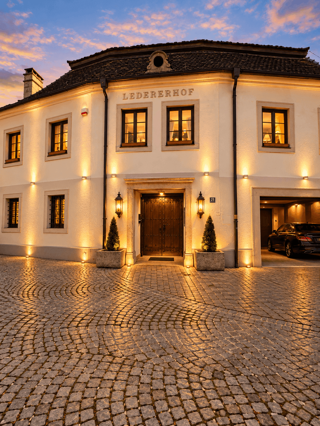 Elegante Gebäudefassade mit beleuchtetem Eingangsbereich, Kopfsteinpflaster und integrierter Garage.