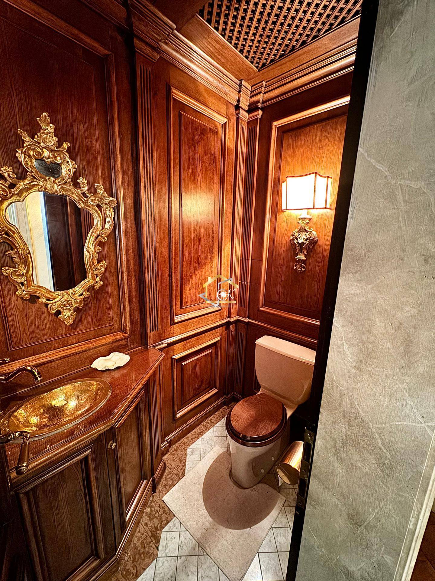 Exklusive Gästetoilette mit dunkler Holzvertäfelung, goldenem Waschbecken und Spiegel.