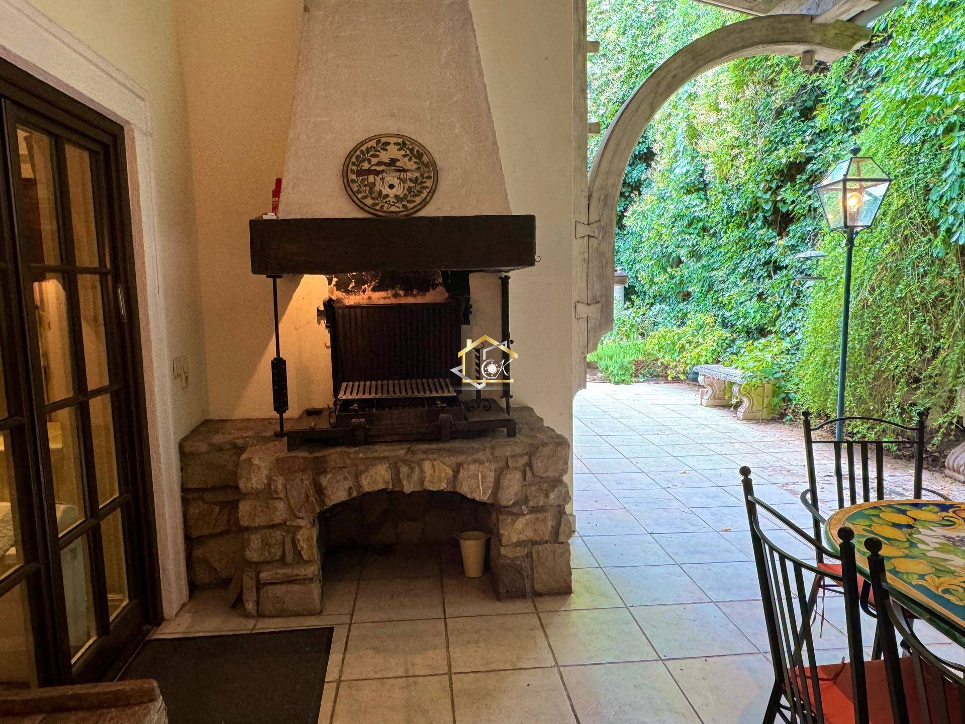 Überdachte Terrasse mit gemauertem Grillkamin und Sitzgelegenheiten im Grünen.