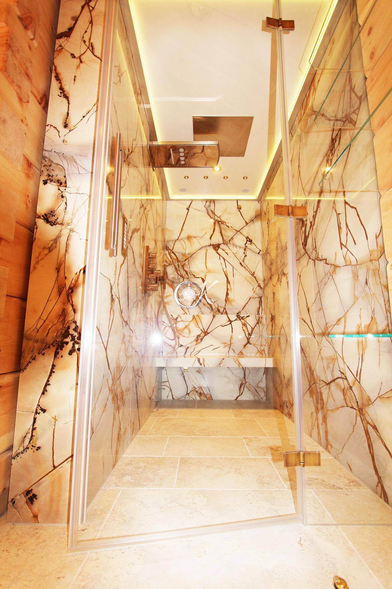 Elegante Duschkabine mit Steinverkleidung und indirekter Beleuchtung in einem luxuriösen Badezimmer.