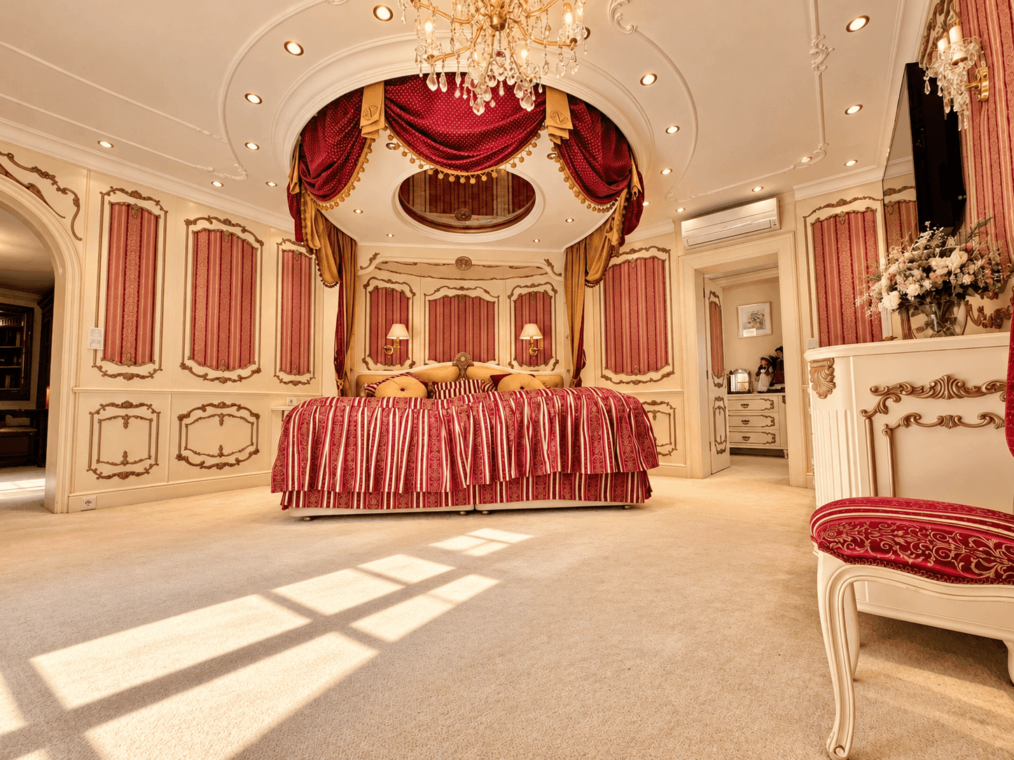 Prunkvolles Schlafzimmer mit opulentem Bett, roten und goldenen Vorhängen, Teppichboden und dekorativen Wandpaneelen.