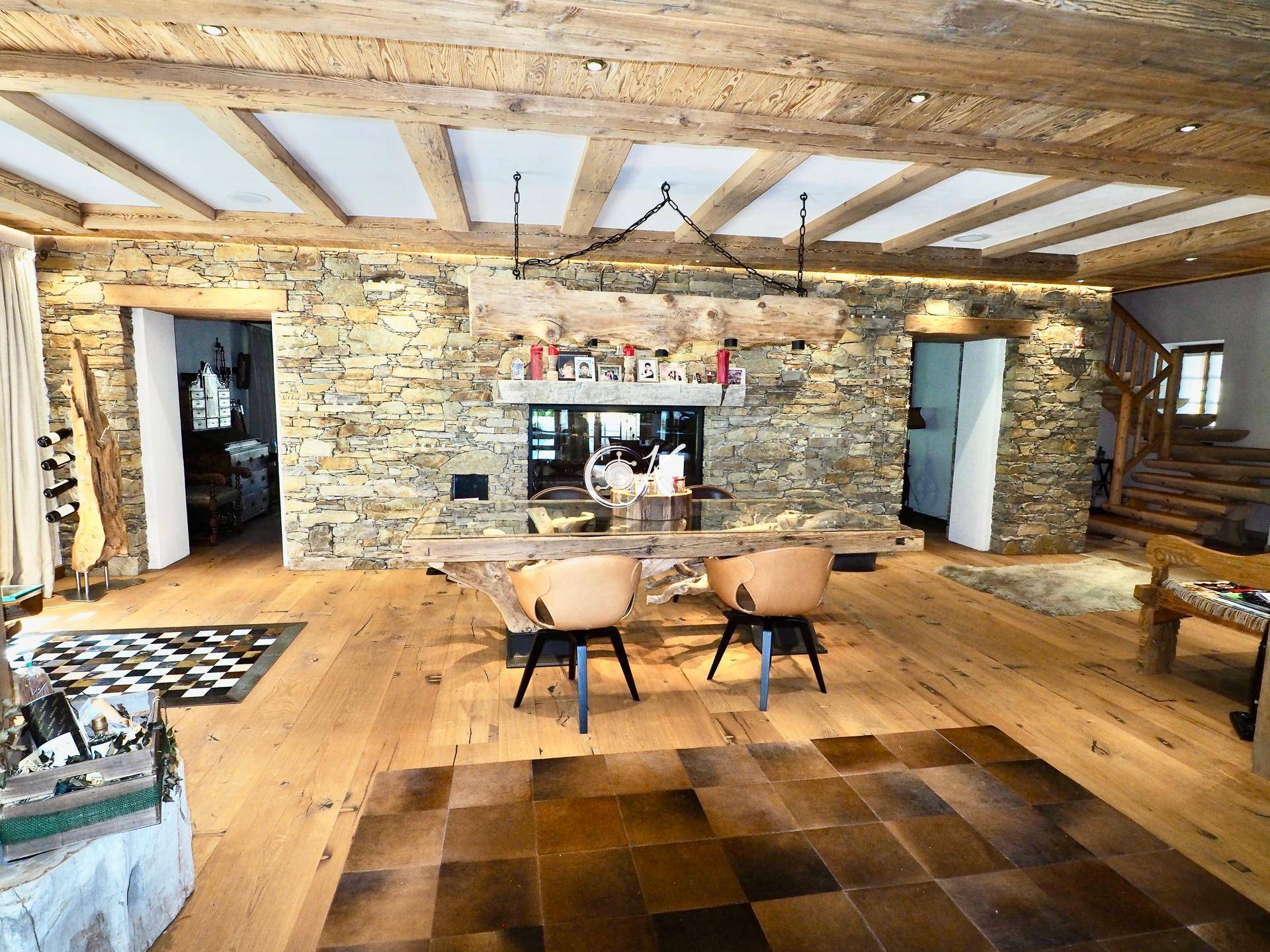 Offener Wohn- und Essbereich mit Holzbalkendecke, Steinwand und rustikalem Holztisch.