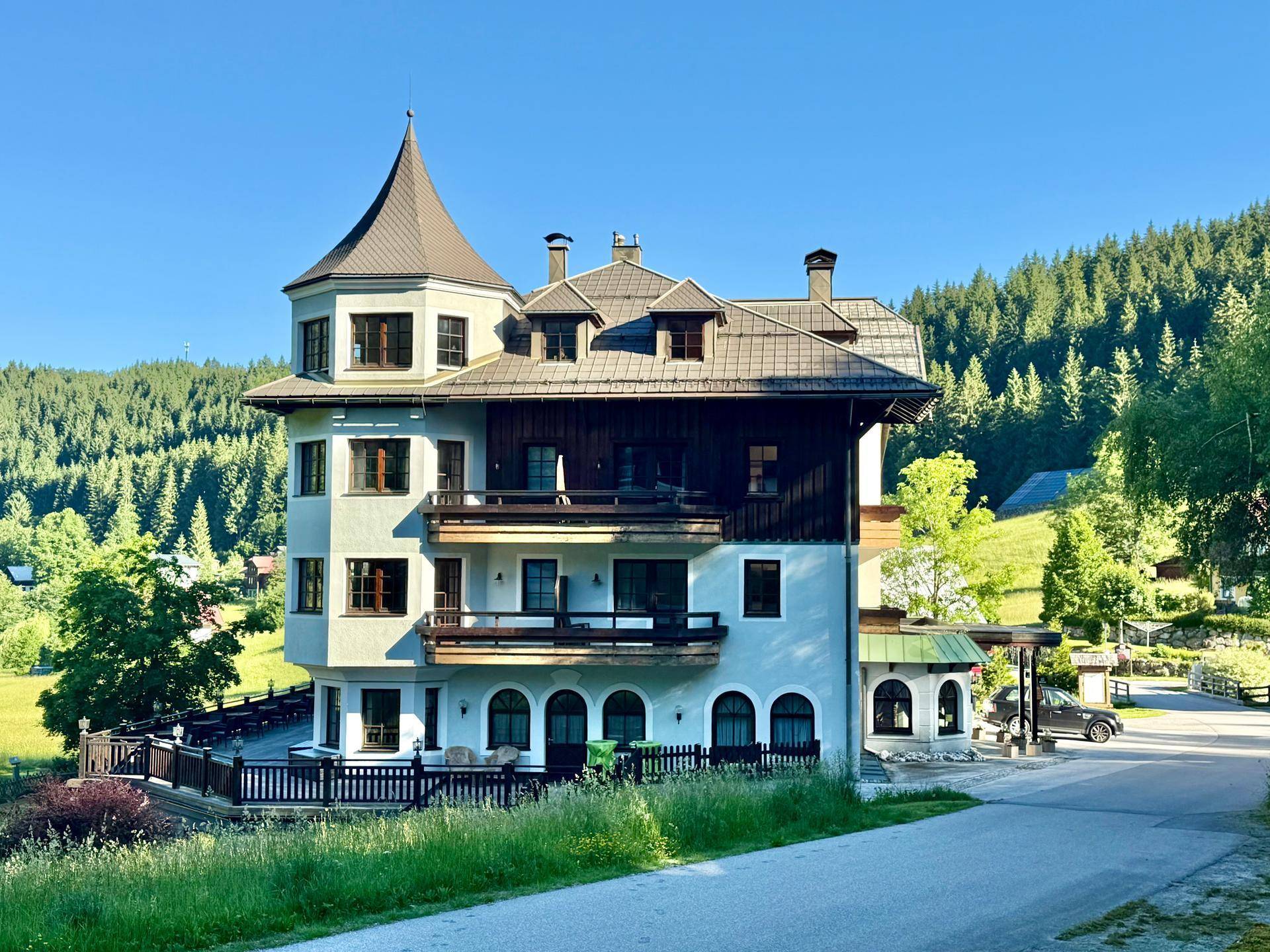 Traditionelles alpines Gebäude mit Turm und Balkonen an einer ruhigen Landstraße.